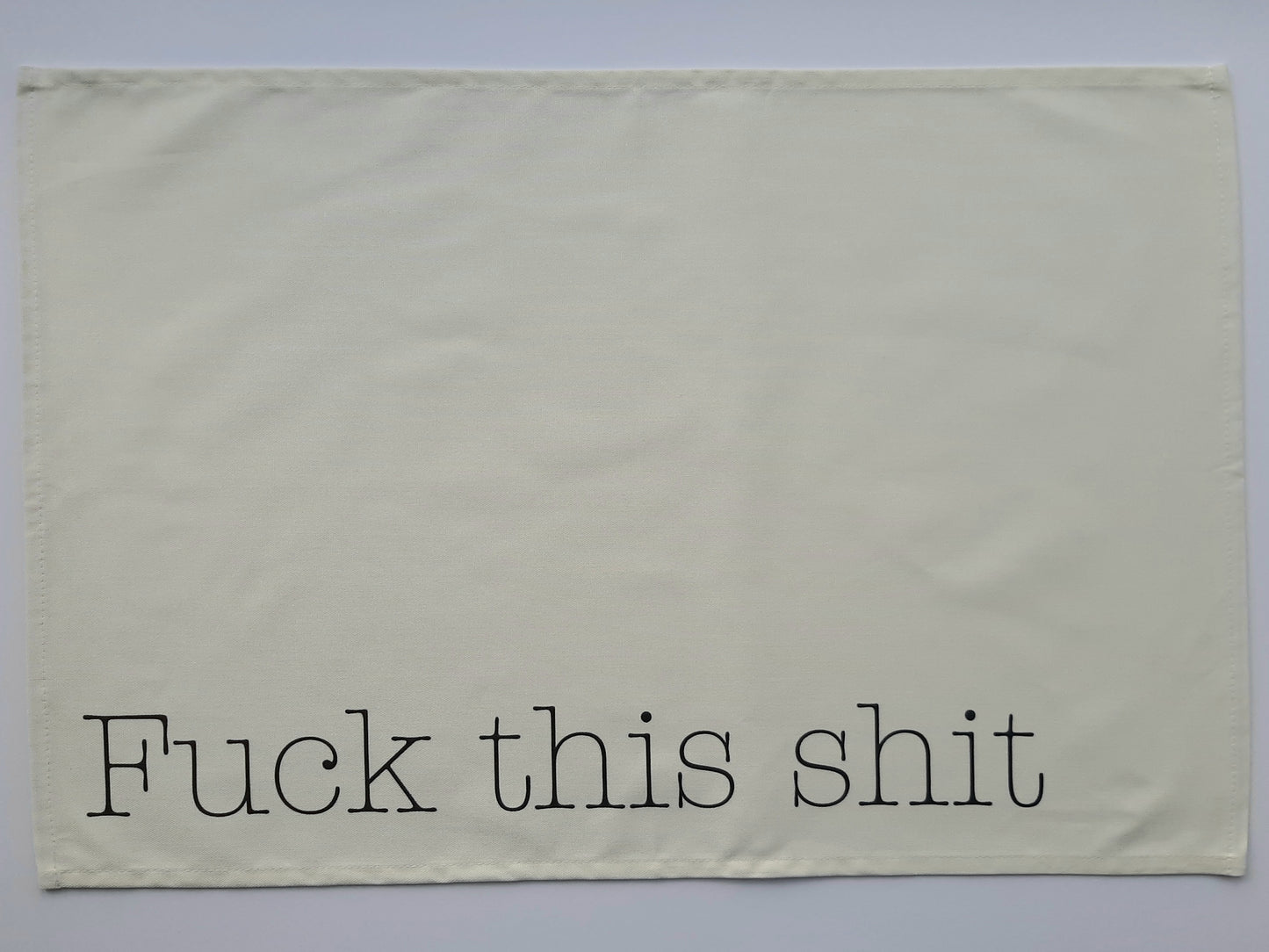 A photo of a tea towel with grey text reading fuck this shit