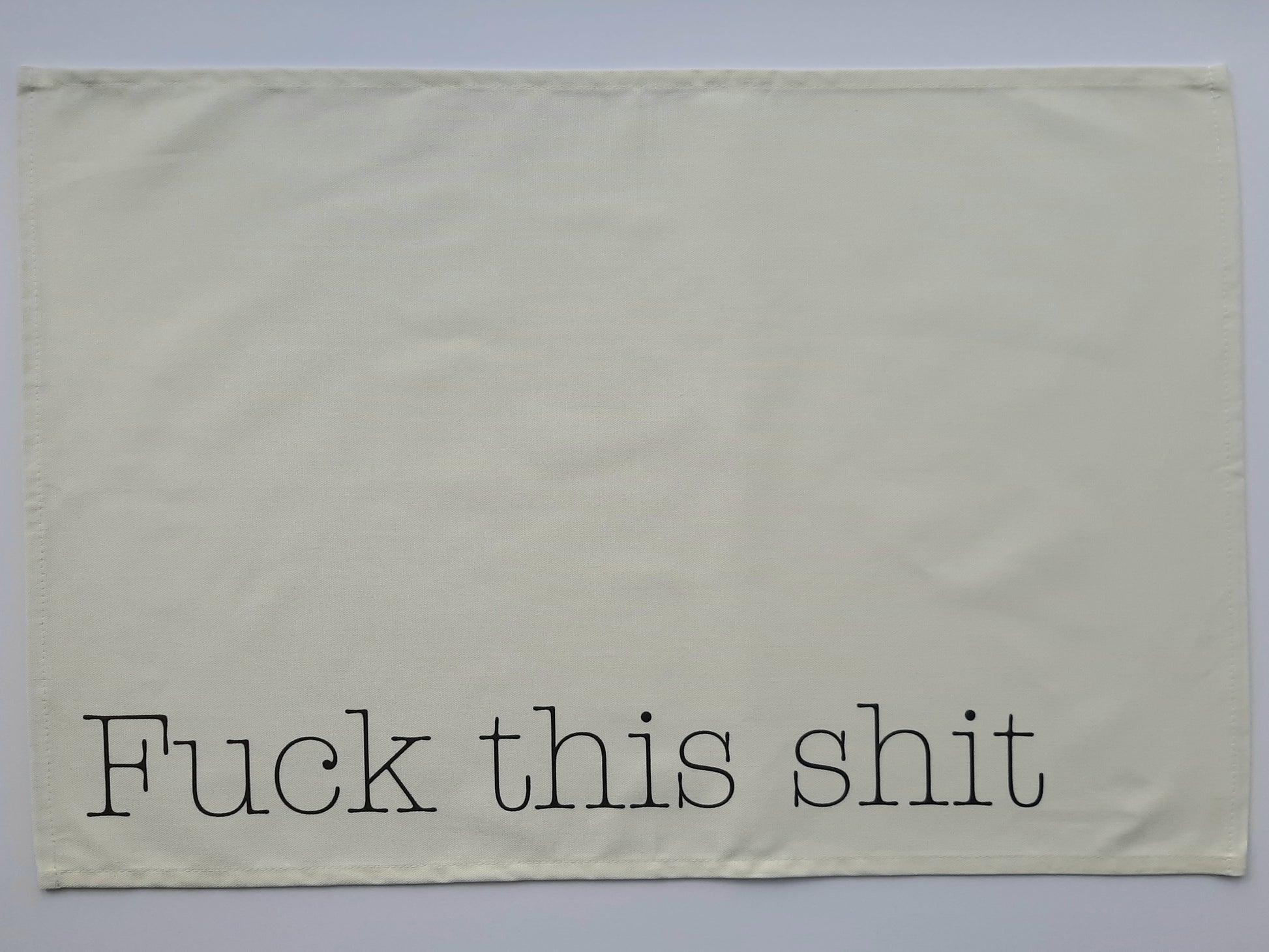 A photo of a tea towel with grey text reading fuck this shit